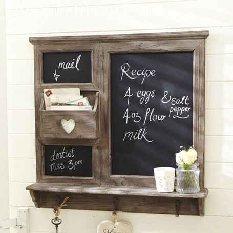 Wall-mounted chalkboard and whiteboard organizer with hooks, baskets, and a small vase of flowers