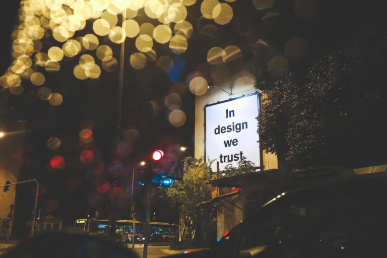 Urban night scene with bokeh lights and a sign reading "In design we trust"