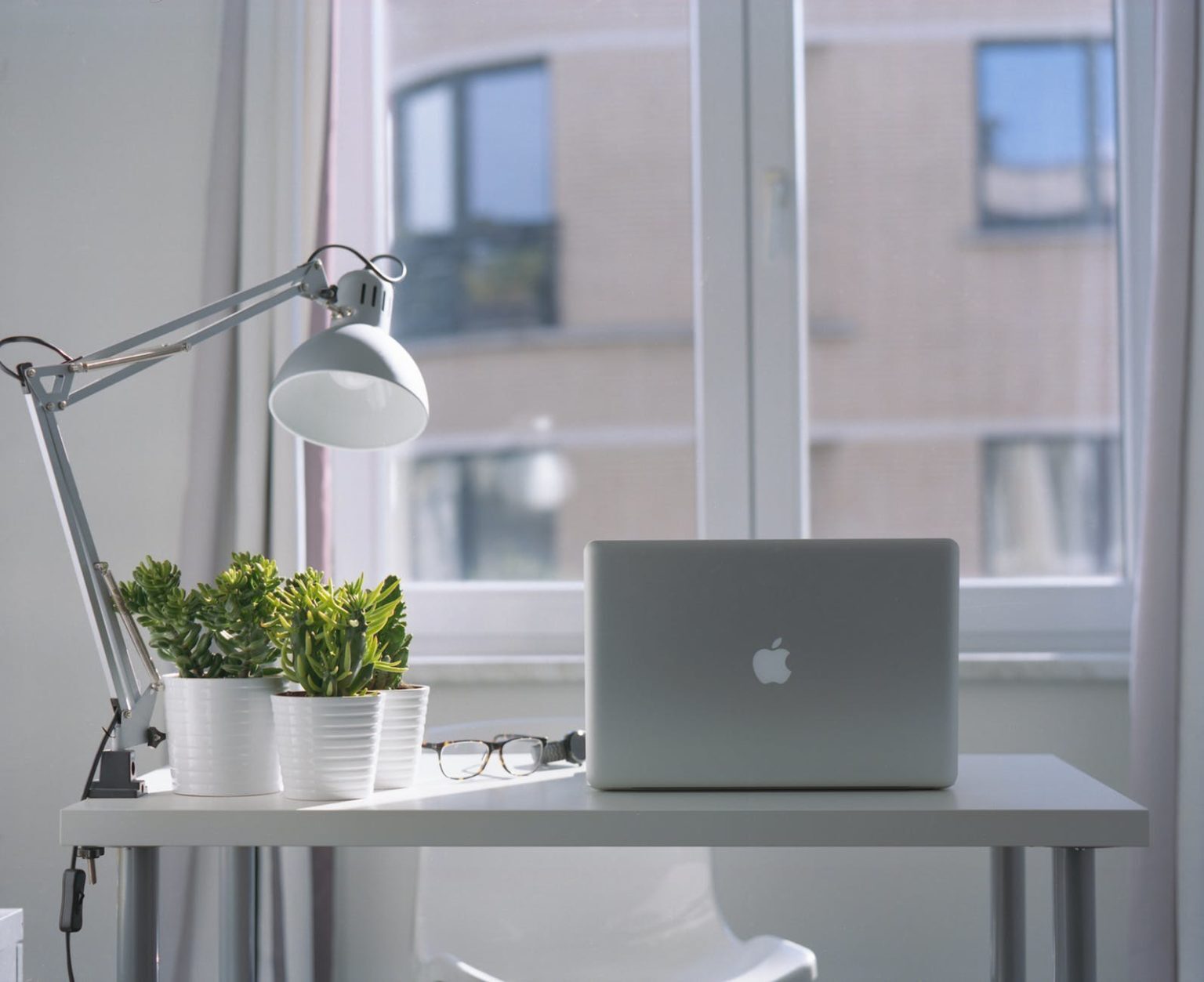 Laptop computer on a wooden table in front of a large window in a home office