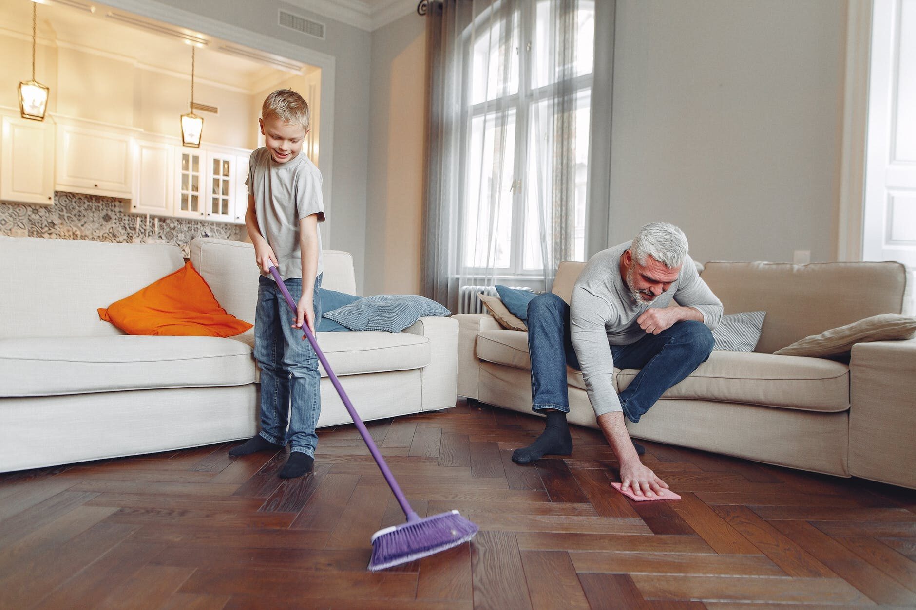Child and woman cleaning a bright living room with a wooden floor and large windows