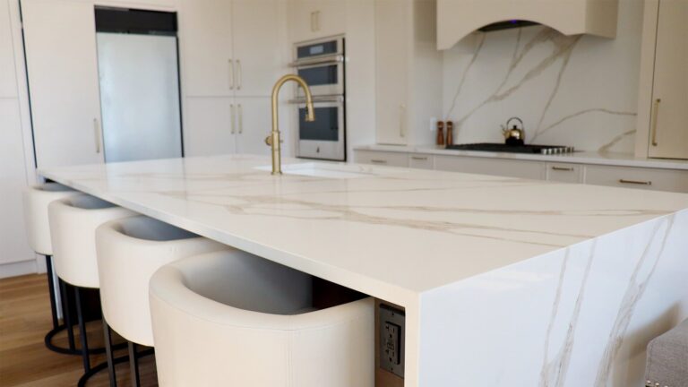 White quartz kitchen island with waterfall edge, integrated seating, and modern brass faucet in a bright winter renovation