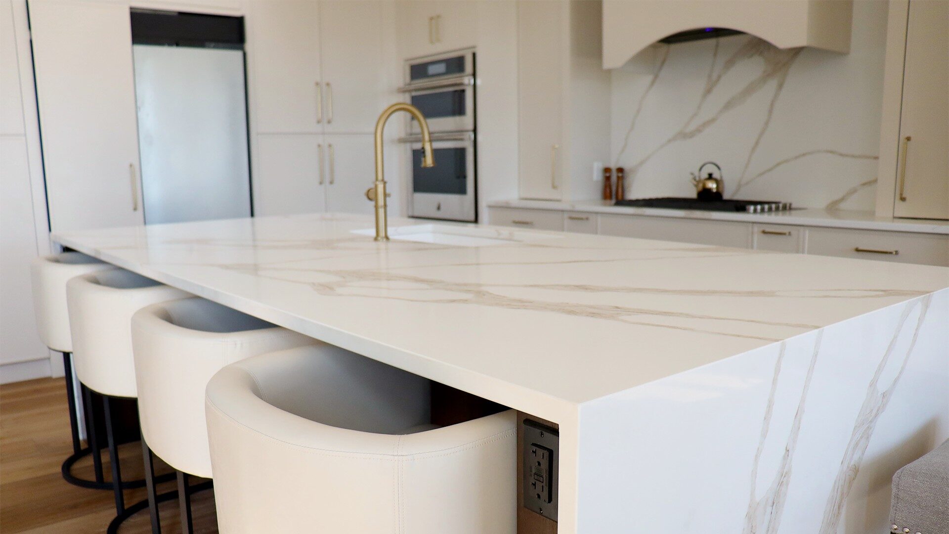 White quartz kitchen island with waterfall edge, integrated seating, and modern brass faucet in a bright winter renovation